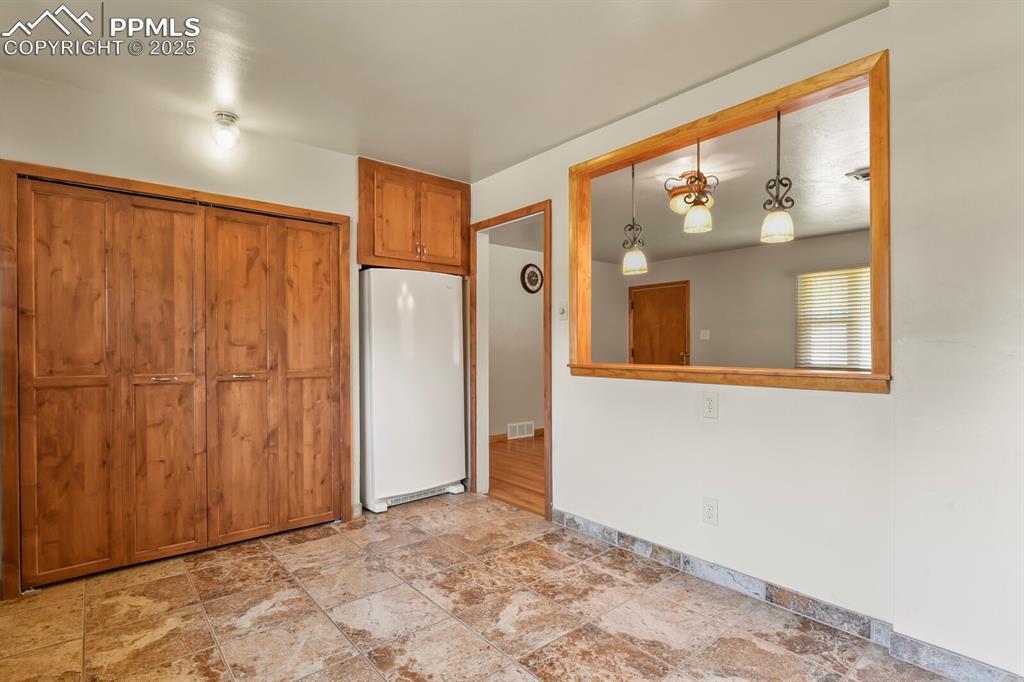 Kitchen featuring laundry/ pantry closet, freestanding refrigerator, solid wood cabinetry, and tile flooring