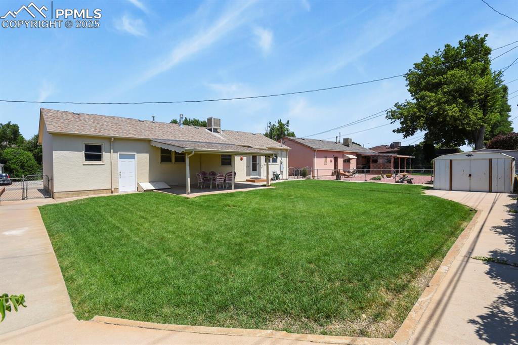 Fenced backyard featuring covered concrete patio, garage access, storage shed