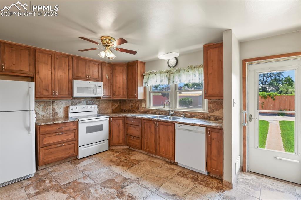 Kitchen featuring white appliances, solid wood cabinetry, backsplash, and ceiling fan