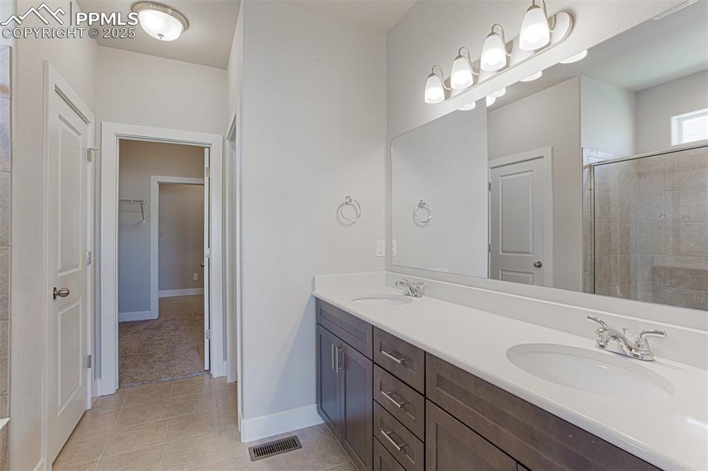 Full bath featuring double vanity, light tile patterned floors, a shower stall, and a walk in closet