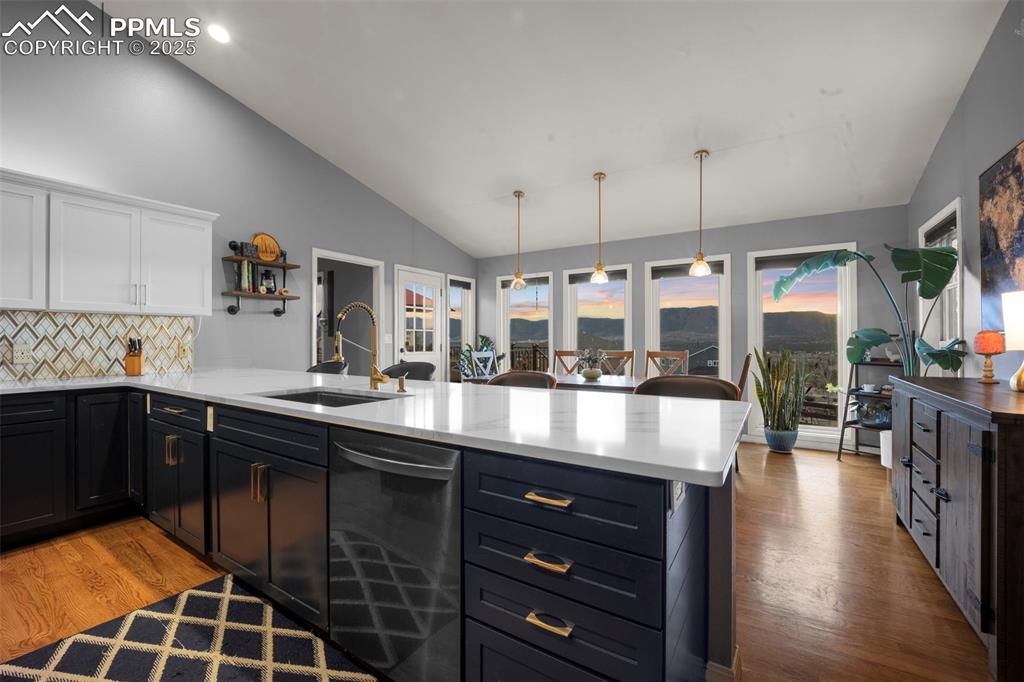 Kitchen with stainless steel dishwasher, white cabinets, a sink, a peninsula, and lofted ceiling