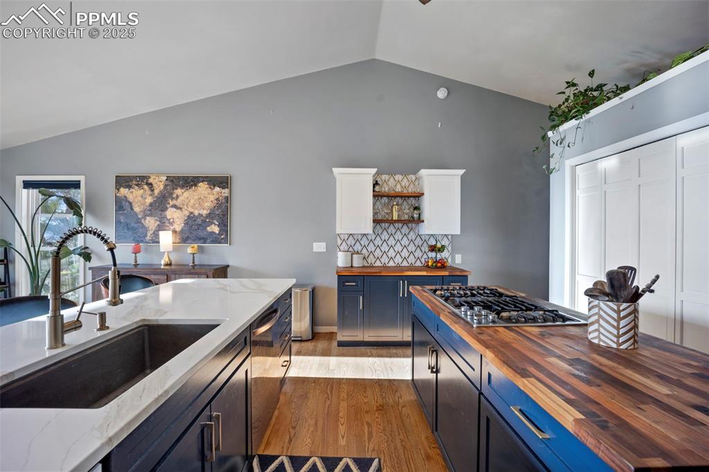 Kitchen with a sink, stainless steel appliances, light wood-type flooring, vaulted ceiling, and wooden counters