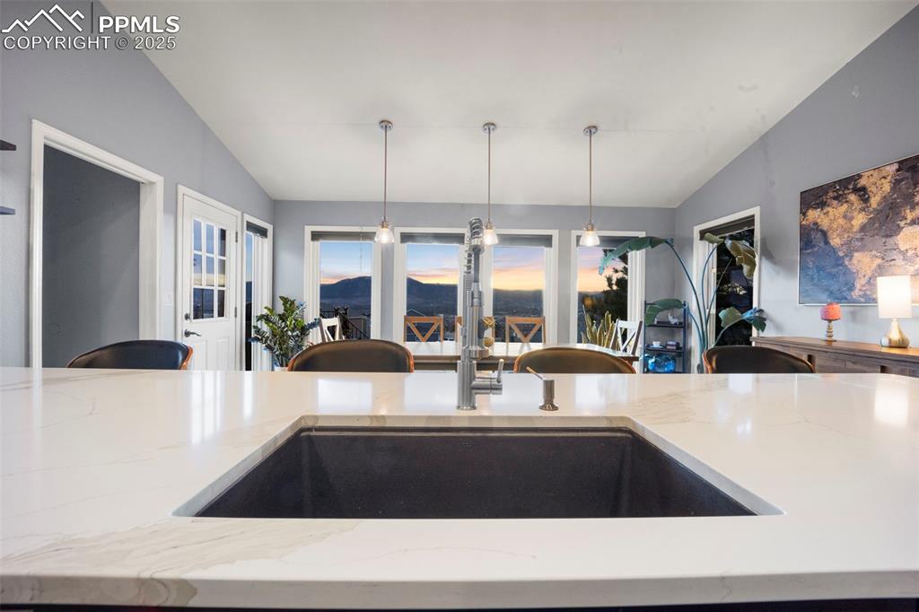 Kitchen with lofted ceiling, light stone counters, decorative light fixtures, and a sink