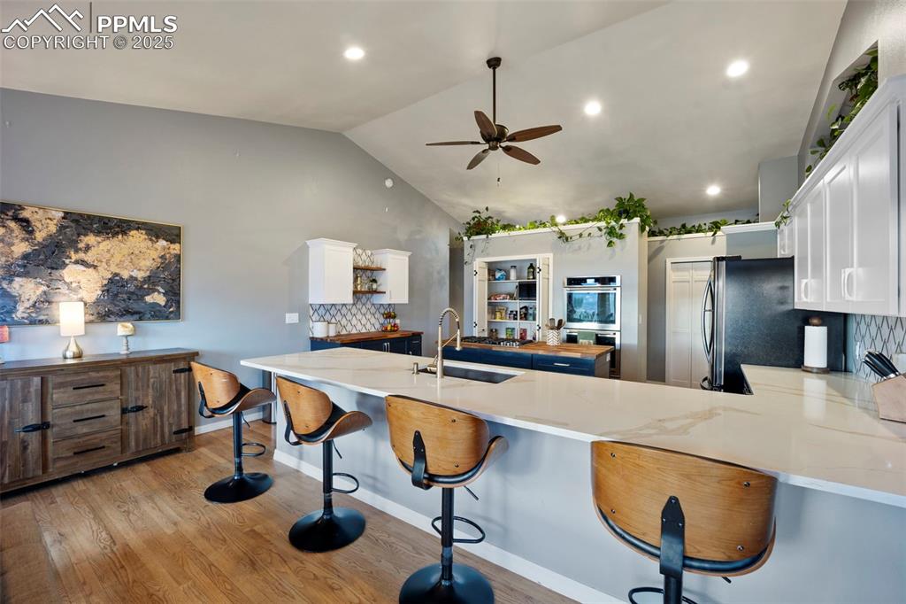 Kitchen with a sink, tasteful backsplash, a ceiling fan, white cabinetry, and appliances with stainless steel finishes