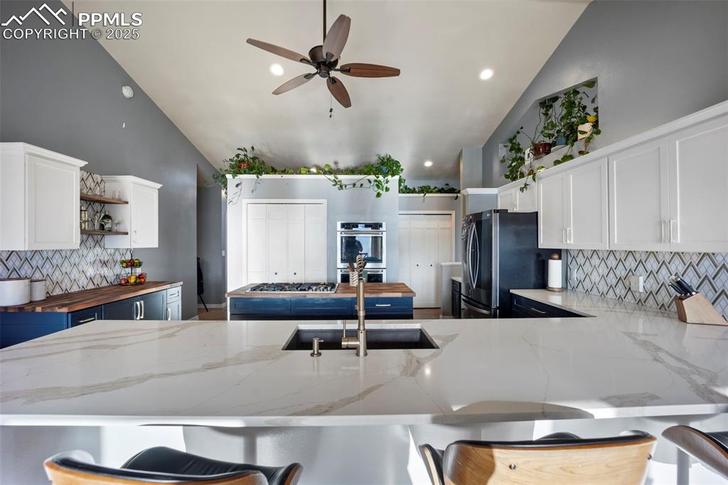 Kitchen featuring a sink, stainless steel appliances, decorative backsplash, high vaulted ceiling, and butcher block counters