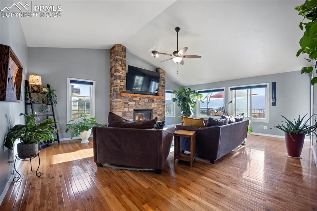 Living room featuring wood-type flooring, a fireplace, baseboards, a ceiling fan, and lofted ceiling