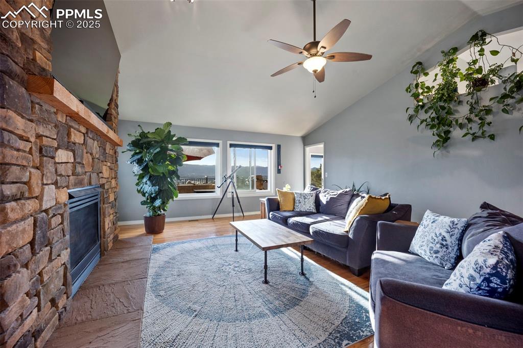 Living room with high vaulted ceiling, wood finished floors, a ceiling fan, and a stone fireplace