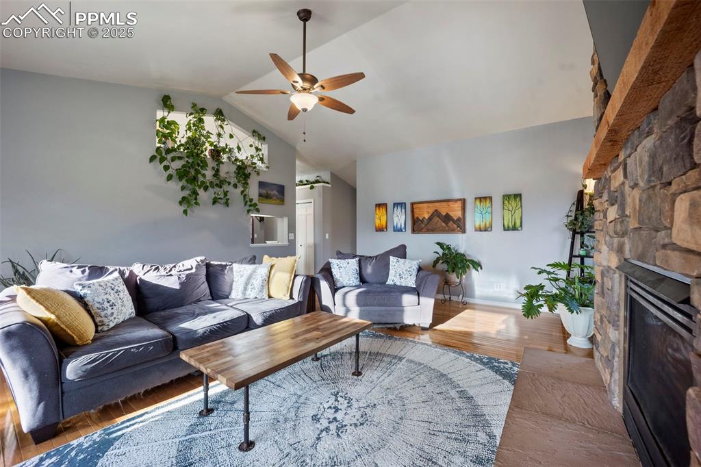 Living area with ceiling fan, vaulted ceiling, wood finished floors, and a fireplace