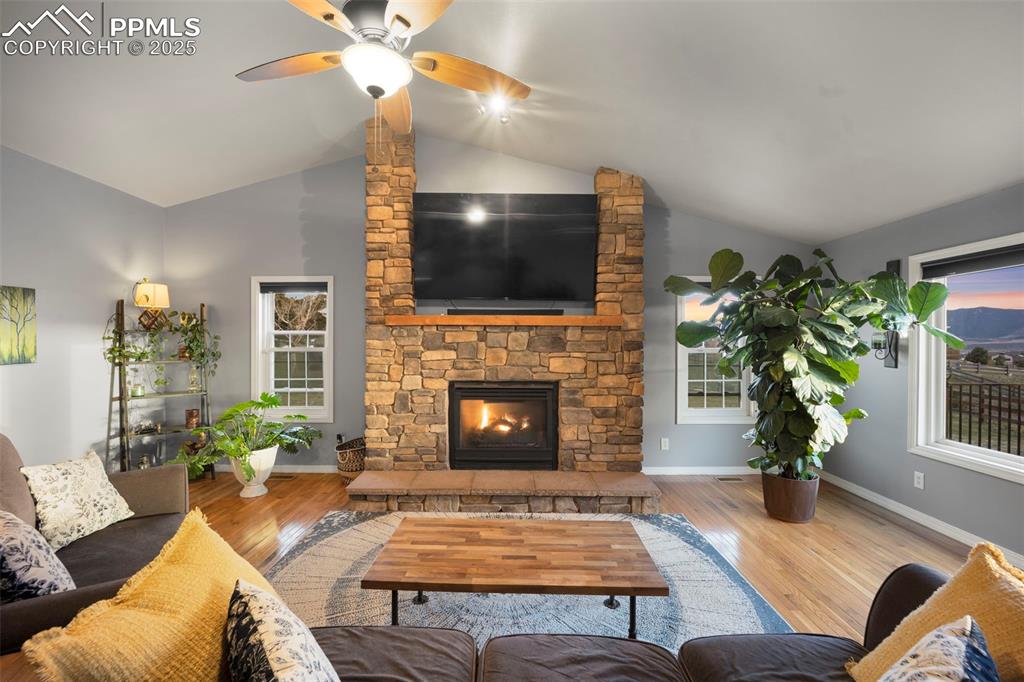 Living area with wood finished floors, ceiling fan, a stone fireplace, and vaulted ceiling