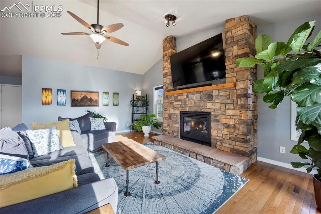 Living room with ceiling fan, hardwood / wood-style floors, baseboards, high vaulted ceiling, and a stone fireplace