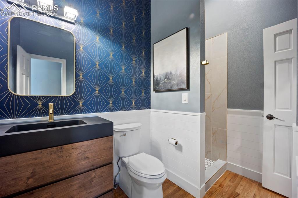 Full bathroom featuring a tile shower, toilet, wood finished floors, vanity, and wainscoting