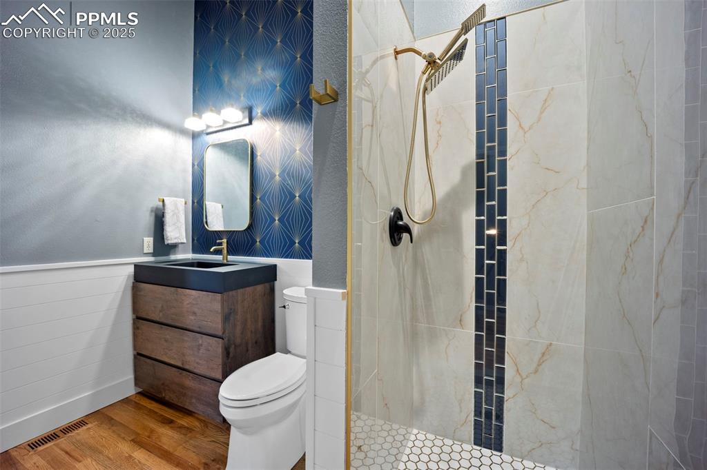 Full bathroom with toilet, visible vents, tiled shower, and wood finished floors