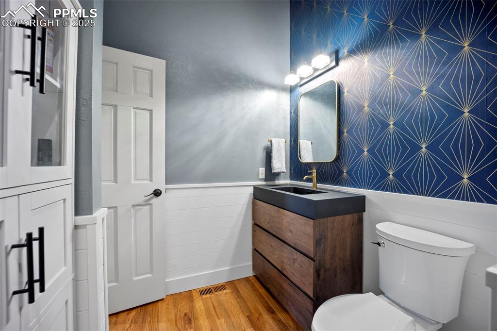 Half bath featuring wood finished floors, wainscoting, toilet, vanity, and visible vents