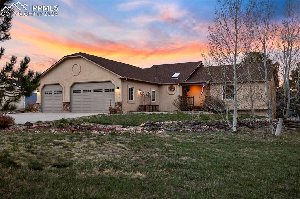 Single story home featuring driveway, stone siding, a lawn, stucco siding, and a garage