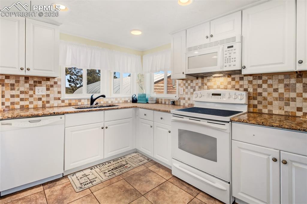 Kitchen with granite counter tops, matching white cabinetry and appliances, tile flooring and nature just out the windows
