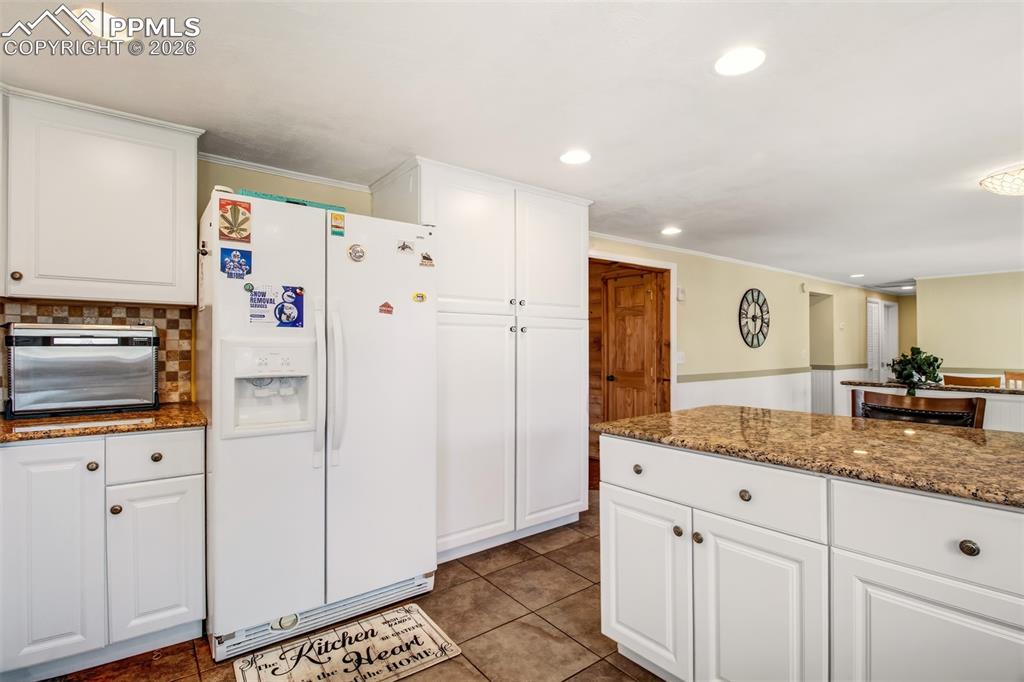 Kitchen with granite counter tops, matching white cabinetry and appliances, tile flooring and nature just out the windows
