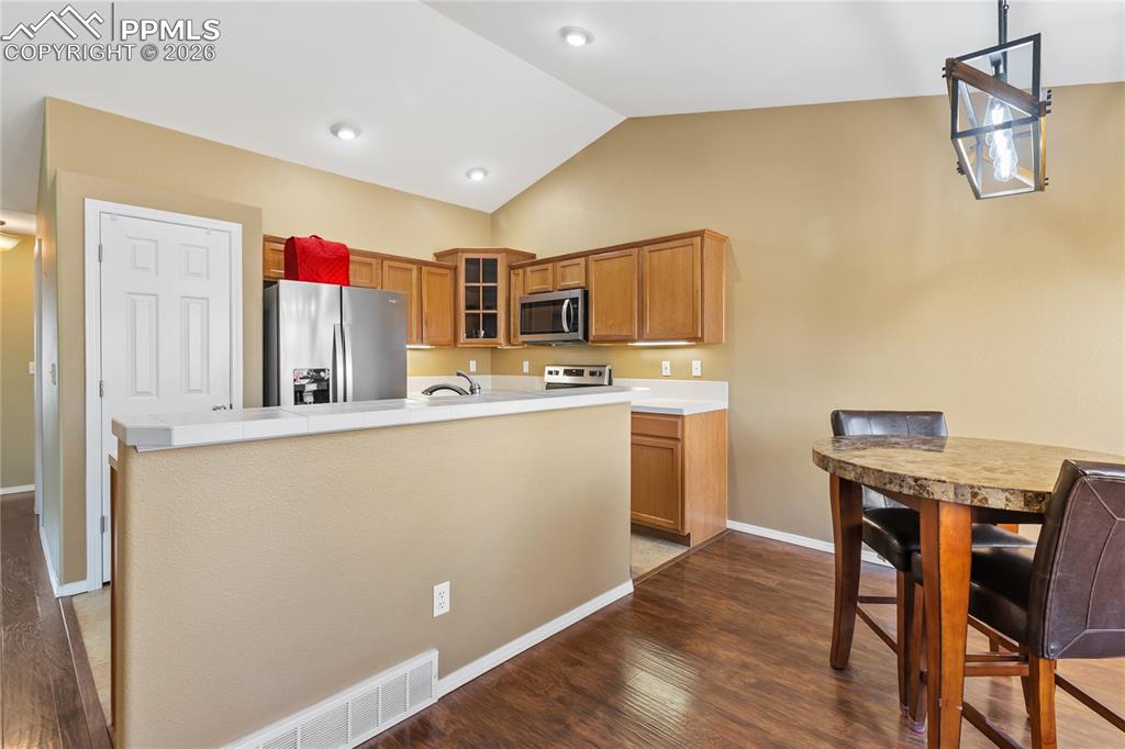 Kitchen featuring glass fronted cabinets, stainless steel appliances, a kitchen island with sink, light countertops, and wood finish cabinetry
