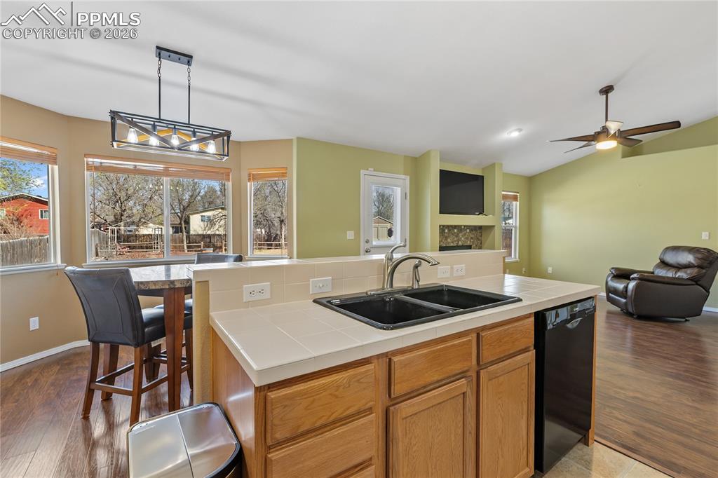 Kitchen with tile countertops, an island with sink, dishwasher, open floor plan, and vaulted ceiling
