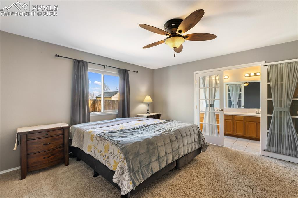 Bedroom featuring light colored carpet, a ceiling fan, french doors, and ensuite bathroom