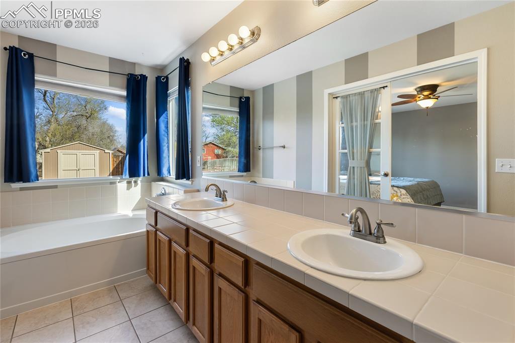 Full bath with ensuite bathroom, double vanity, a bath, ceiling fan, and light tile patterned flooring