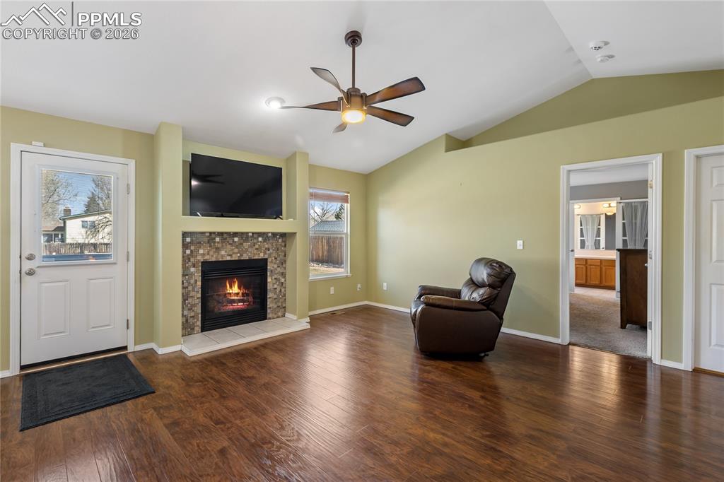 Unfurnished room featuring dark wood finished floors, a ceiling fan, a fireplace, and vaulted ceiling