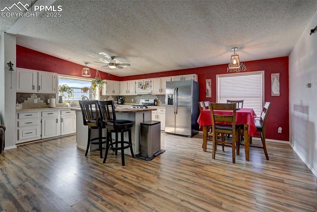 Kitchen with white cabinets, stainless steel appliances, a textured ceiling, light wood-style floors, and a breakfast bar area