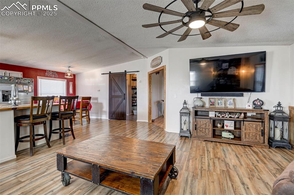 Living area featuring a barn door, a textured ceiling, light wood-type flooring, a ceiling fan, and lofted ceiling