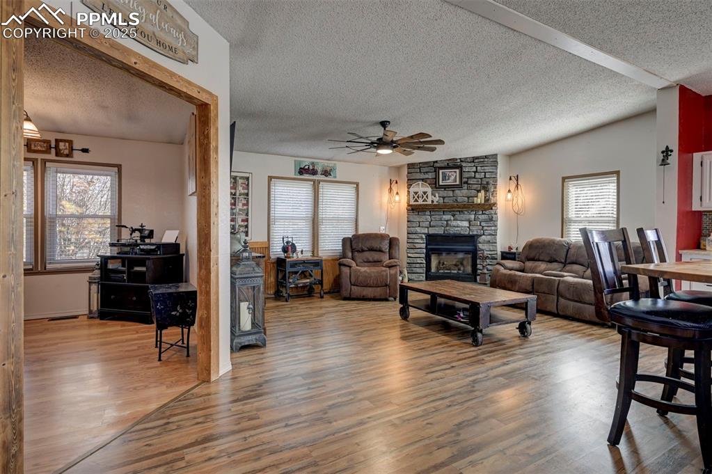 Living room with a textured ceiling, a stone fireplace, light wood finished floors, and a ceiling fan