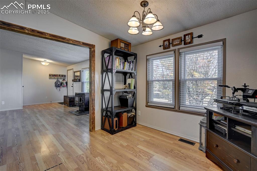 Home office with a textured ceiling, a wood stove, light wood-style flooring, and a chandelier