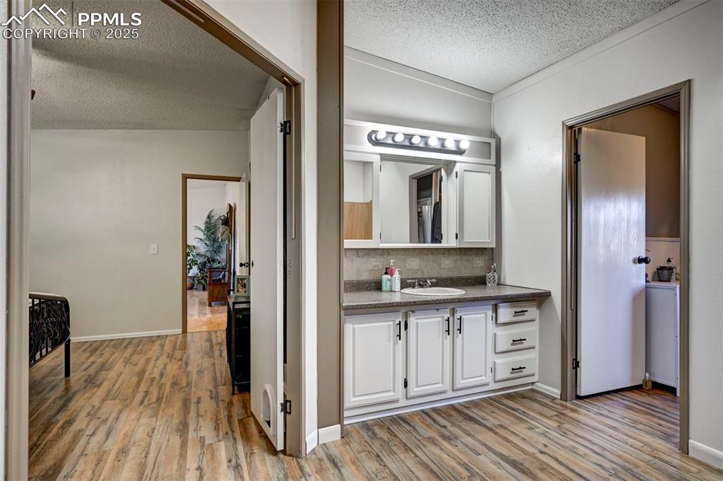 Bathroom with a textured ceiling, light wood-style floors, vanity, and decorative backsplash