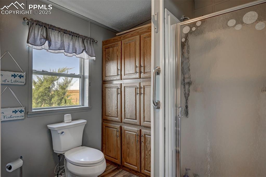Full bath featuring a textured ceiling, a shower stall, and wood finished floors