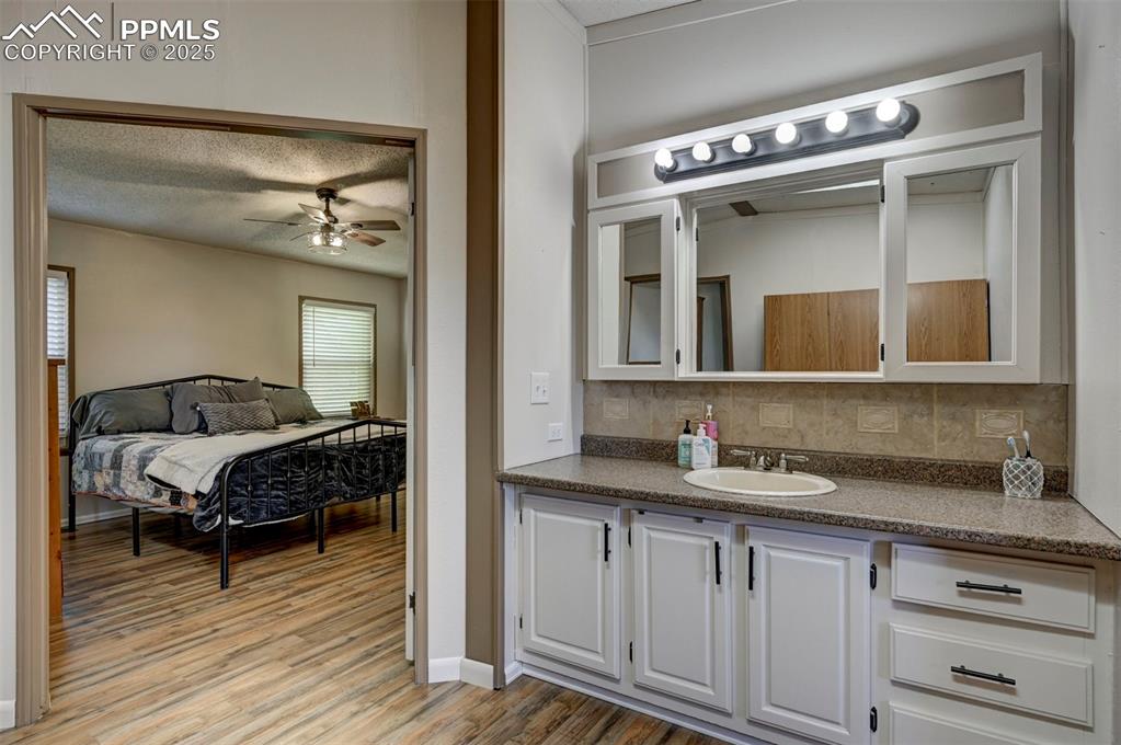 Ensuite bathroom with a textured ceiling, vanity, backsplash, light wood-style flooring, and a ceiling fan