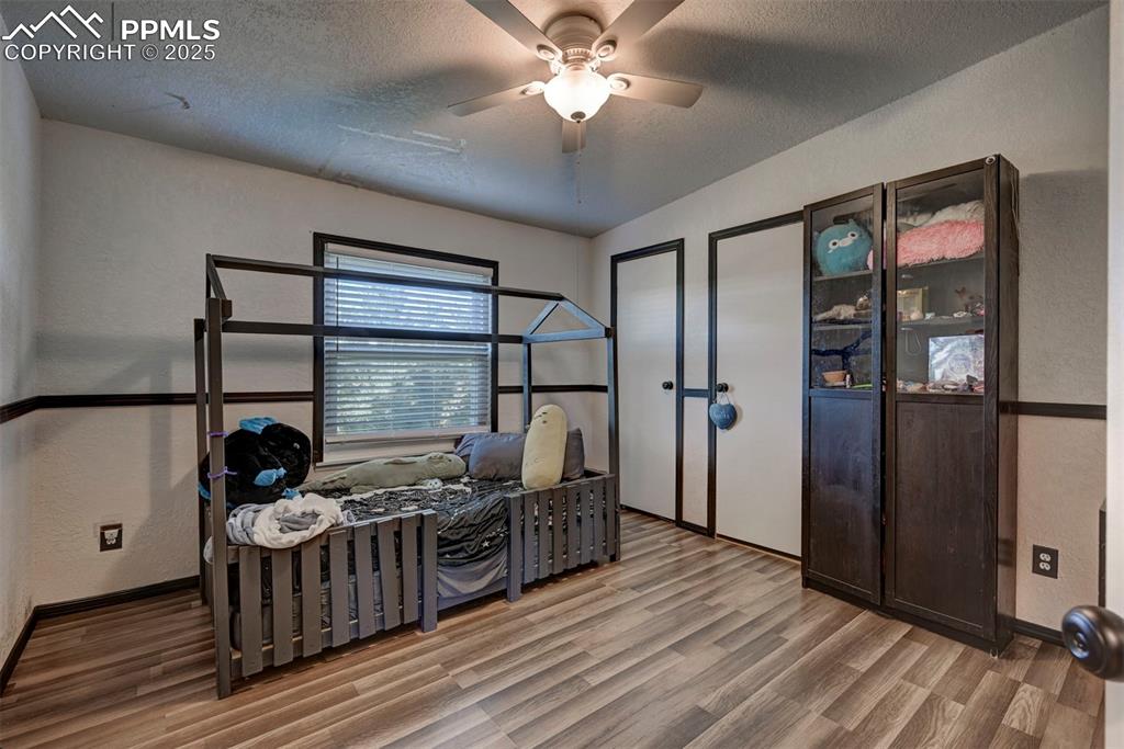 Bedroom with a textured wall, a textured ceiling, a ceiling fan, and wood finished floors