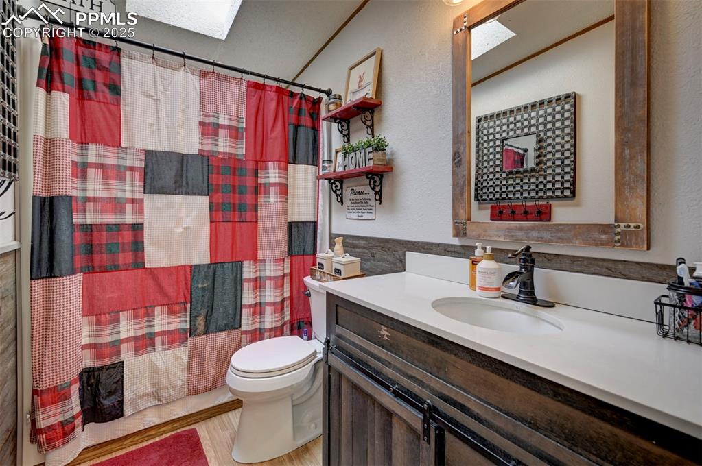 Full bath featuring a skylight, shower / bath combo, vanity, light wood-style flooring, and tile walls