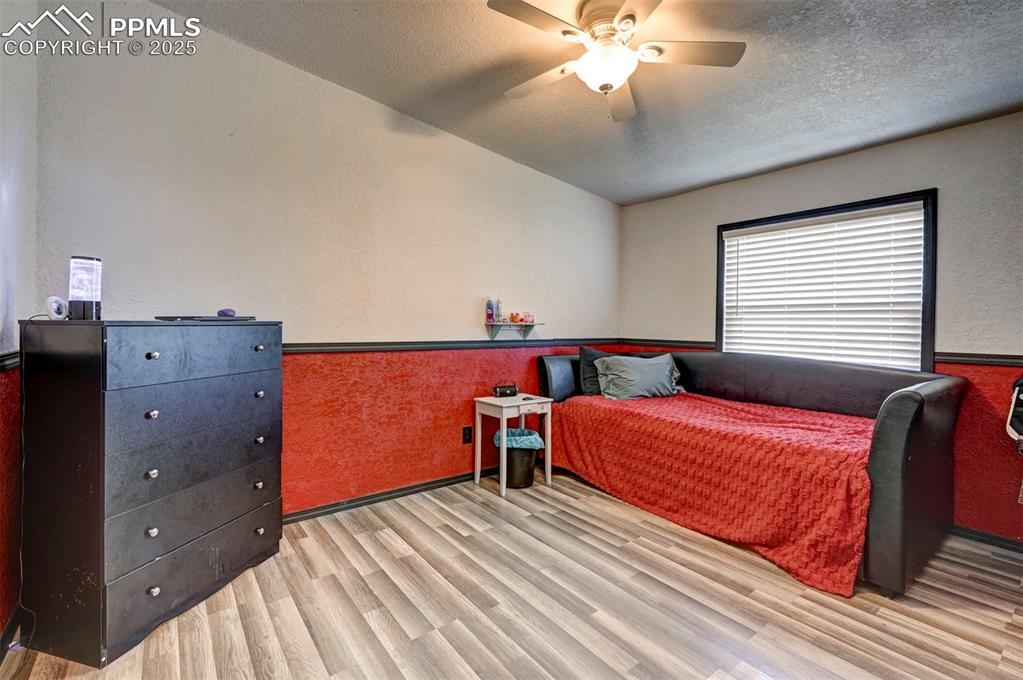 Bedroom featuring wood finished floors, ceiling fan, a textured wall, a textured ceiling, and wainscoting