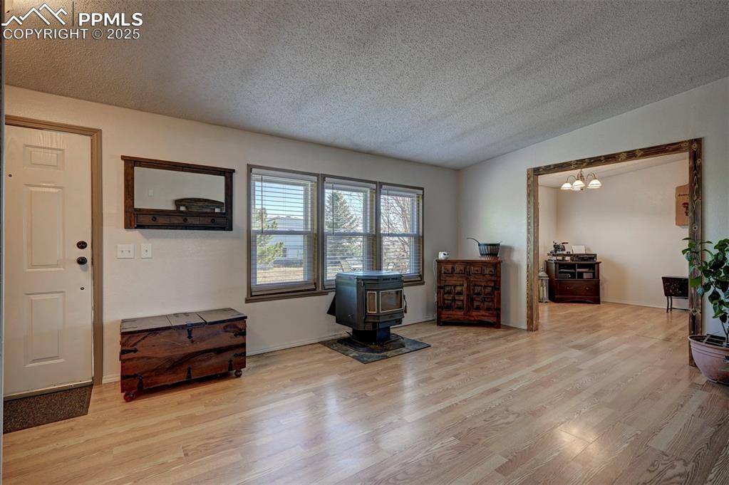 Living area featuring a textured ceiling, wood finished floors, a wood stove, vaulted ceiling, and a chandelier