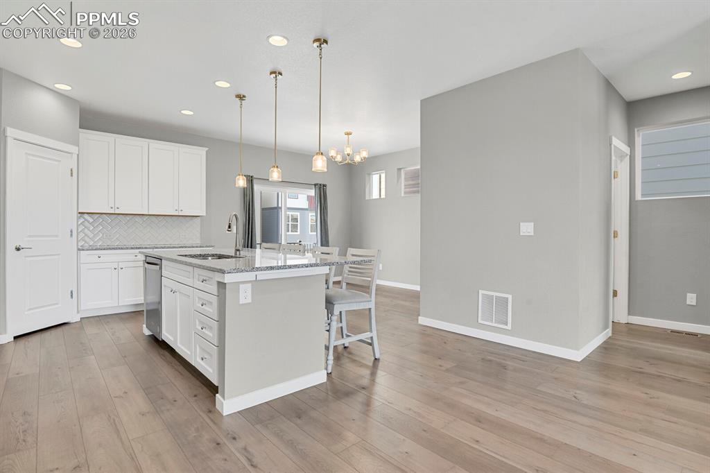 Kitchen with white cabinetry, light stone counters, recessed lighting, a kitchen island with sink, and decorative light fixtures