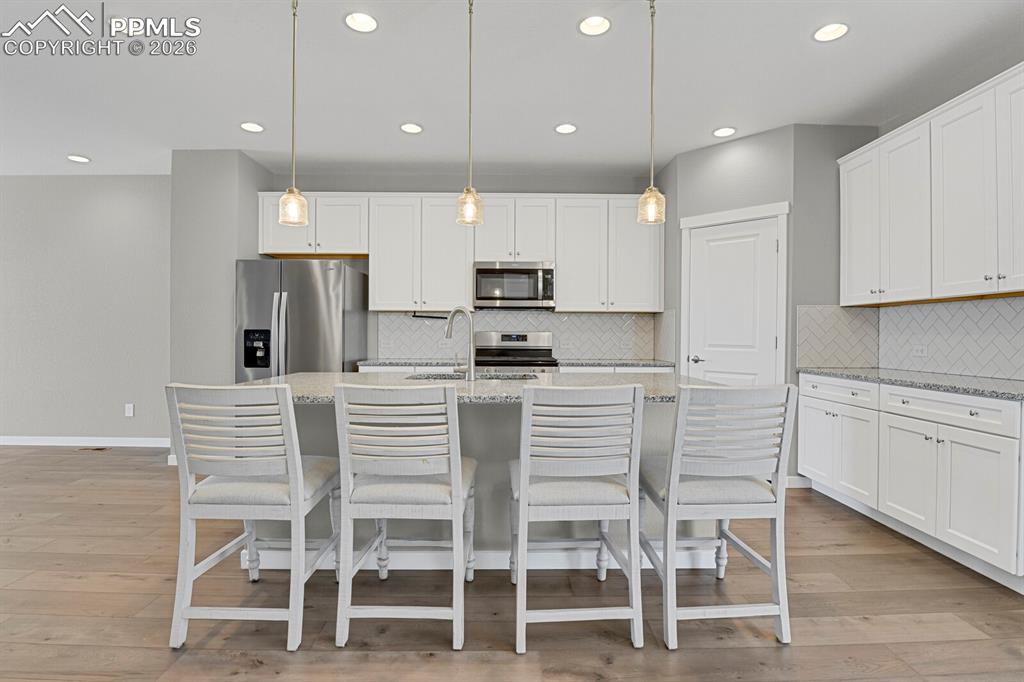 Kitchen featuring appliances with stainless steel finishes, white cabinets, decorative light fixtures, Breakfast bar 