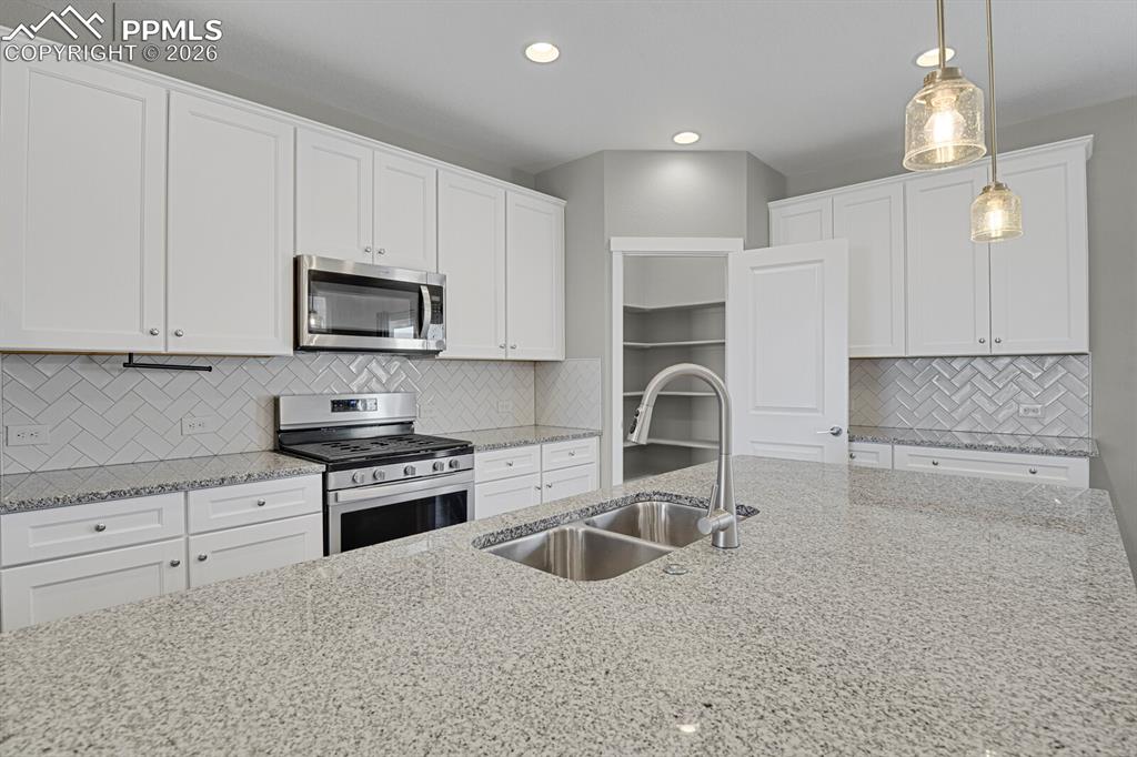 Kitchen featuring stainless steel appliances, light stone countertops, white cabinetry, and recessed lighting