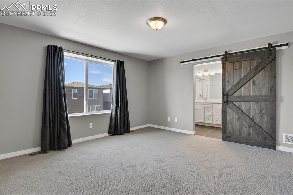 Unfurnished bedroom featuring a barn door, light colored carpet, and connected bathroom