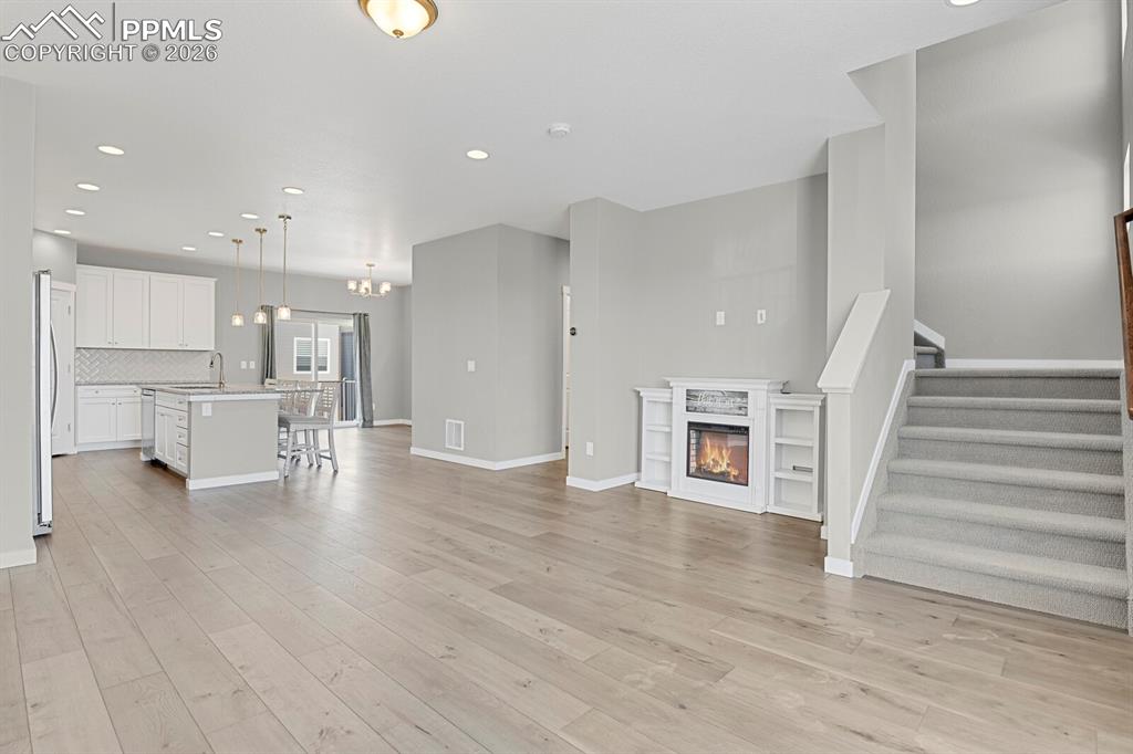 Unfurnished living room with a stand alone Electric glass covered fireplace, recessed lighting, and stairs leading to the upper level 