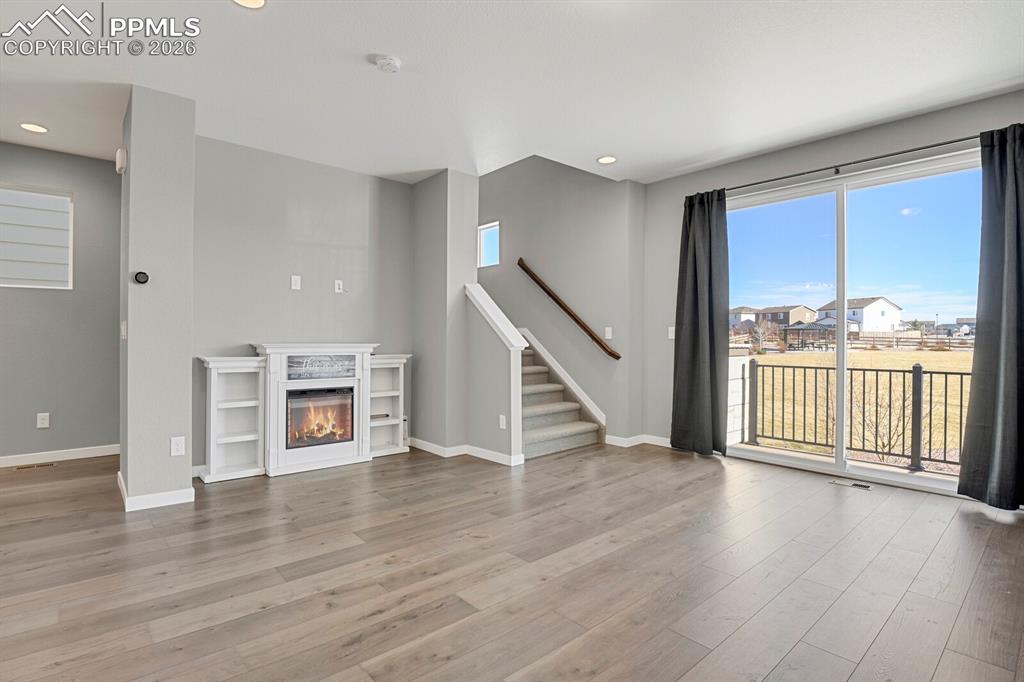 Unfurnished living room featuring a glass covered fireplace, stairway, light wood-style flooring, and recessed lighting