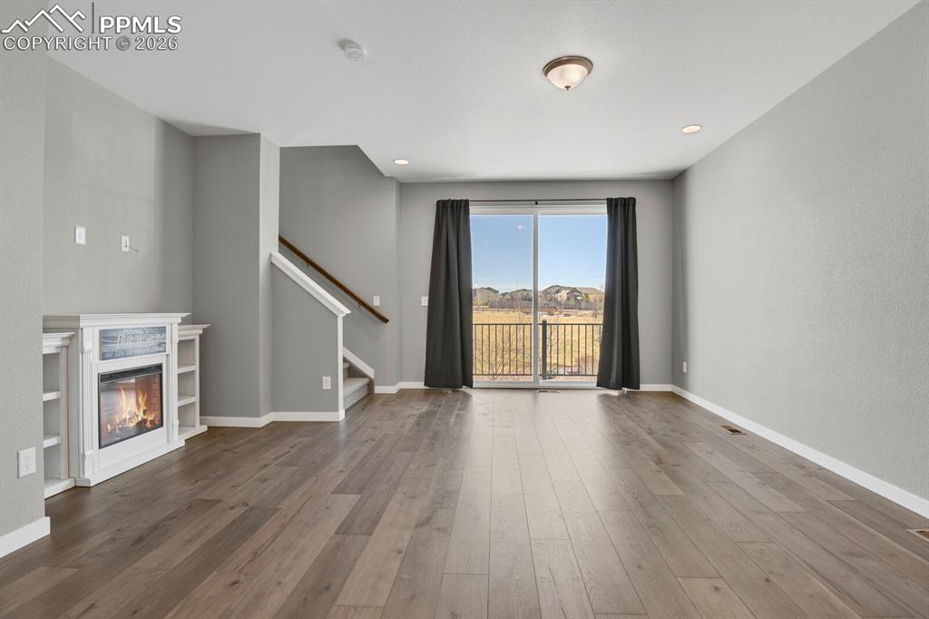 Unfurnished living room with a glass covered fireplace, wood finished floors, stairs, and recessed lighting