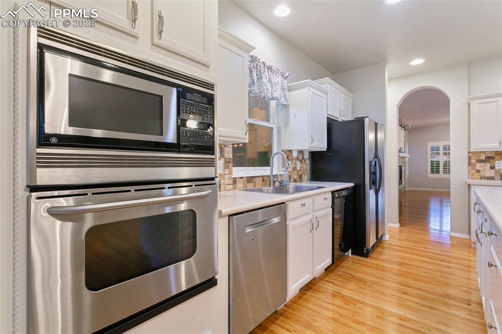 Kitchen with appliances with stainless steel finishes, arched walkways, tasteful backsplash, white cabinets, and recessed lighting