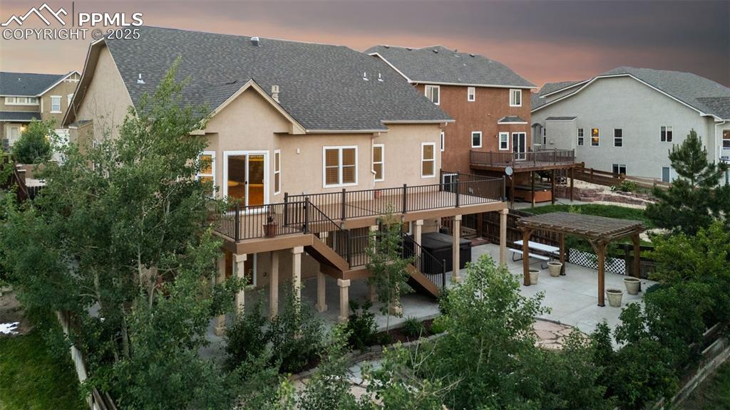 Back of property at dusk featuring stairs, a patio area, a wooden deck, stucco siding, and a shingled roof