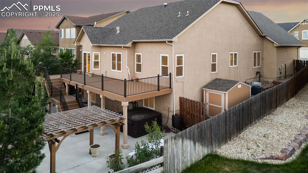 Back of house at dusk featuring a hot tub, stucco siding, a fenced backyard, a wooden deck, and roof with shingles