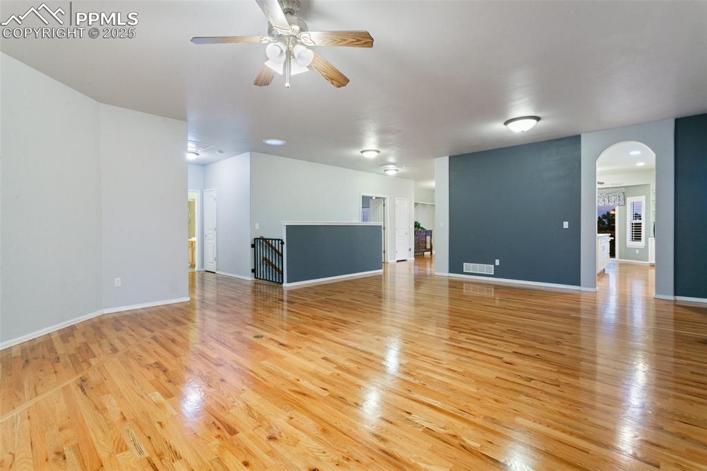 Unfurnished living room with light wood-style flooring, arched walkways, and ceiling fan