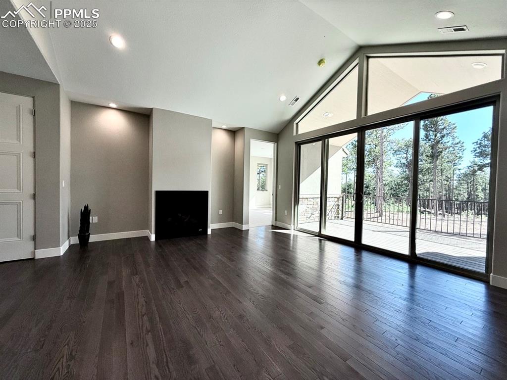 Vaulted Living Room with Large Windows, Oversized Sliding Doors to the Covered Composite Deck, Gas Fireplace, and Wood Flooring.