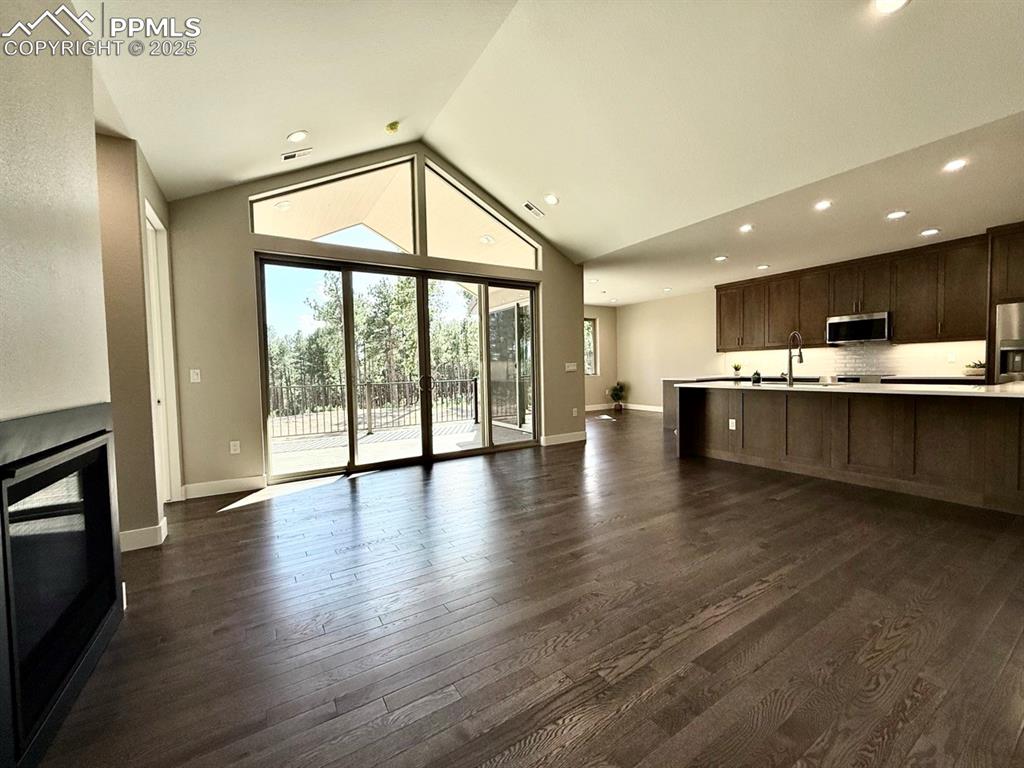 Vaulted Living Room with Large Windows, Oversized Sliding Doors to the Covered Composite Deck, Gas Fireplace, and Wood Flooring.