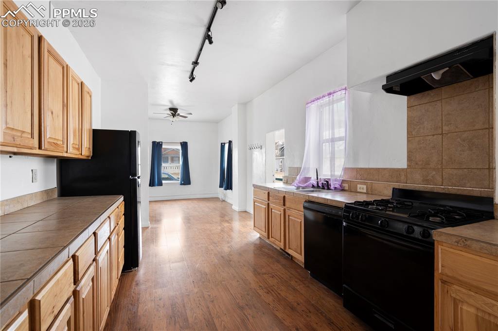 Kitchen with black appliances, track lighting, exhaust hood, dark wood-style floors, and ceiling fan